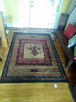 Full view of the Saudi Arabian rug on wooden flooring, showing the entire design including borders and central figure.