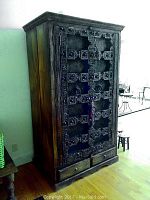 Front view of closed armoire showing carved shutter doors and metal ring pulls.