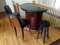 Photo showing the bar table with black top, two padded black leather chairs with wooden backs and one tufted black stool.