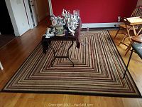 Full view of Shaw accent rug under a table with decorative items on top, showcasing size and multicolor striped pattern.