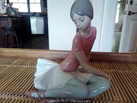 Front angle view of Lladro ballerina figurine seated with arms resting, showing glossy porcelain finish and pastel colors.