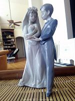 Front angle view of porcelain figurine showing bride holding baby and groom standing beside her.
