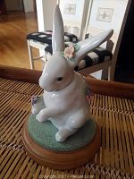 Front view of white porcelain rabbit figurine with flower decorations on a wooden base.