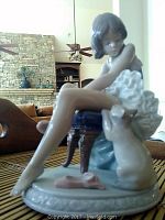 Side angle view showing the girl sitting on a dark wooden chair with cat and teddy bear beside her, placed on a round base.