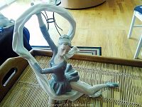 Full view of Lladro ballerina porcelain figurine sitting on a woven surface, showing the extended arms forming a loop with fabric.
