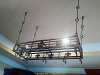Full view of the hanging metal kitchen pot and pan rack suspended from ceiling by four chains with hooks.