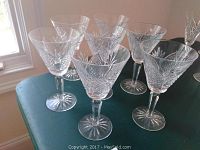 Seven Waterford crystal stemware glasses arranged on a green surface, showing intricate cut patterns on bowls and starburst base design.