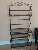 Front view of the metal mesh shelving unit showing black paint, mesh shelves, and decorative scrolls on sides and top.