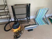Photo showing the vacuum, fan, and three chairs together on the floor next to a metal shelving unit.
