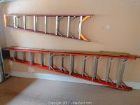 Two aluminum extension ladders leaning against a garage wall