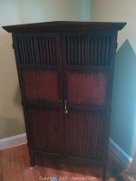 Front view of dark wood entertainment cabinet with two vertically slatted doors and a locking mechanism.