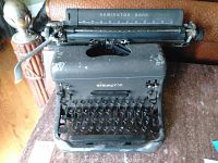View of the entire Remington Rand vintage typewriter showing the black metal body, round keys, and signs of wear.