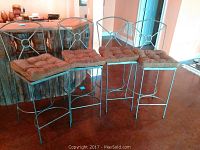 Four matching metal frame bar chairs with brown tufted seat cushions arranged in a row in front of a bar setup.