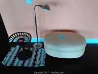 Floor lamp, ottoman, metal chair, and rug arranged against a black floor and white wall