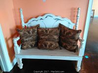 Front view of white carved wood bench with three wildlife-themed throw pillows seated on it, showing detailed carvings on bench and texture of pillows.