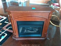 Front view of gas fireplace with wooden mantel showing detailed craftsmanship and glass front with logs inside.
