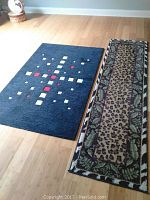 Both rugs laid out side by side on wooden flooring, showing the blue geometric area rug and the leopard print runner with leaf border.