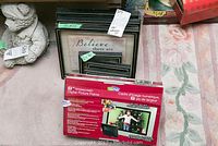 Photo showing multiple stacked framed decorative art pieces with one visible 'Believe there are' framed print and an 8-inch widescreen digital picture frame in its original box by GiiNii.