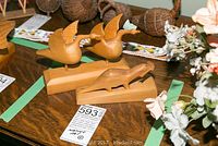 Two wooden native art carvings shown on wooden table, one carving of two ducks in flight on single base, and another otter holding fish on base.