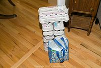 Stack of egg cartons next to a blue reusable shopping bag on a wooden floor