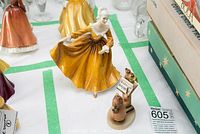 Photo of a porcelain figurine of a woman in yellow dress with small separate figurine showing a person with music sheet and birds