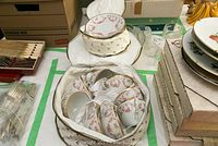 Set of 8 teacups and 8 matching saucers, stacked inside a padded fabric carrying case, showing the floral pattern and gold trim.