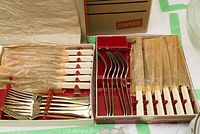 Two boxes of vintage cutlery showing forks and knives with white handles protected in paper wrapping inside the boxes.