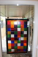 Overall front view of stained glass panel hung by chains showing full colored grid pattern.