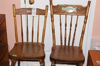 Front view of two mismatched wooden pressback chairs showing their seats, legs, and backrests with carved details