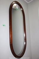 Front view of the tall oval mirror with wooden frame mounted on the wall.