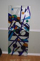 Full view of the unframed stained leaded glass panel standing upright against the wall, showing entire panel and geometric colored design.