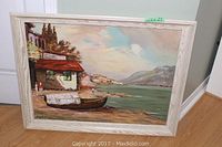 Full view of the oil on board coastal landscape painting by D E Boocock, showing the scene with boat, buildings, water, and mountains, framed in light wood.