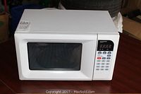 White Magnasonic microwave oven placed on a wooden surface, showing front and top sides, including a clear window on the door and digital control panel on the right.