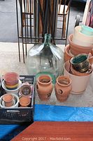Full lot view showing demi john, assorted planters stacked, metal trellises, and shepherd hooks leaning against a board.