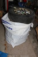 Four used Yokohama radial tires mounted on alloy rims stacked vertically with plastic wrapping around them.