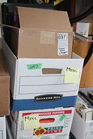 Photo showing stacked boxes labeled Misc and Bankers Box, including open top box with visible books