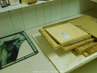 Photo showing several wooden stained glass work boards stacked on a white table with wood grain paneling background.