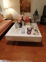Photo showing the coffee table in a living room setting with various decorative items on top (items not included in sale). Table has a glossy white Arborite top and dark faux wood base.