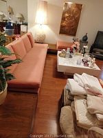 Left profile view of salmon-pink fabric sofa on wooden base alongside orange bench and accessories