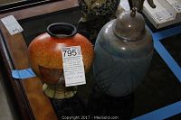 Two ceramic vases side by side on a table; one orange with bamboo design and the other blue with a lid and metallic finial.