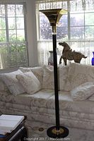 Full view of the gold colored and black metal floor lamp positioned next to a sofa.