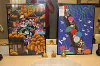 Pair of framed Pan Xiaoling paintings side by side on countertop, showing harvest festival and fair themes