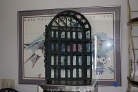 Metal wine rack in front of framed poster on a shelf.