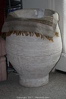 Full view of large white textured resin vase with fringed rug draped on top