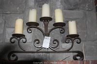 Metal candle holder with five beige pillar candles placed on a stone background.