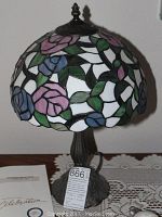 Pair of Tiffany style leaded glass lamps, showing floral stained glass shades and bronze bases, placed on wooden table with lace doily.