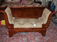 Side angle view showing floral fabric upholstery and carved wooden armrests of vintage chaise lounge.