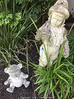 Photo showing the full boy statue and smaller teddy bear statue together outdoors among plants.