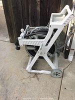 White resin garden hose reel cart from side showing wheels, handle and hose wound on reel.
