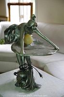 Front view of full lamp showing female figure leaning over shell tray and glass globe, power cord coiled around base.